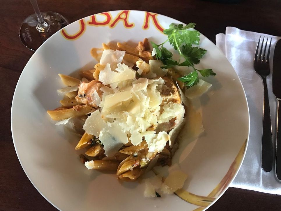 Nudeln mit Parmesan in einem Suppenteller, daneben Messer und Gabel auf einer weißen Stoffserviette.
