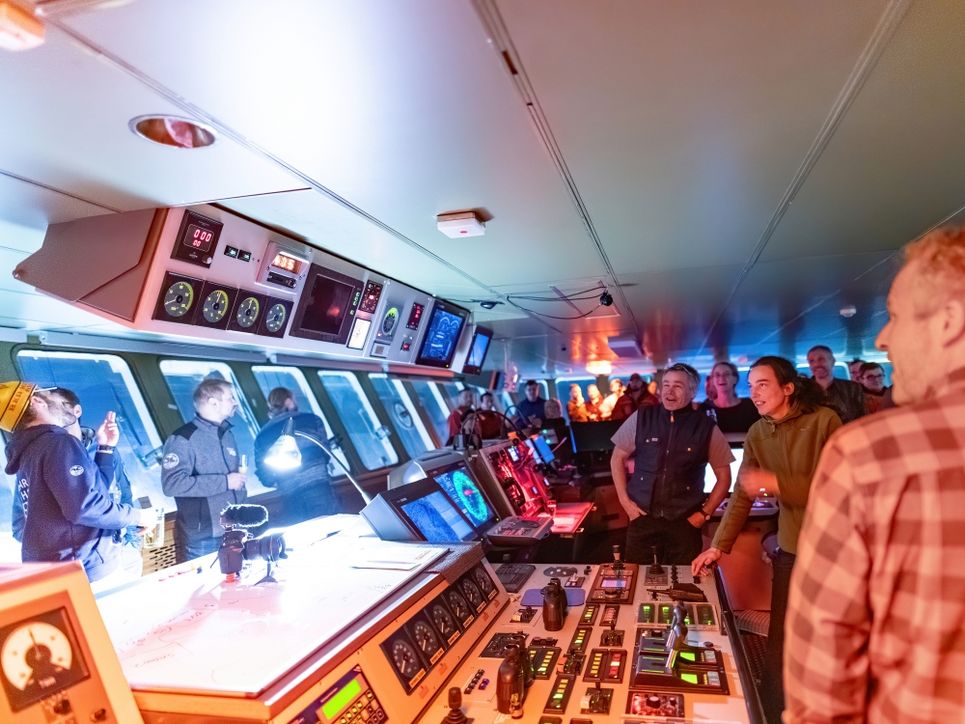 Viele Personen in einem Raum mit Apparaturen, Bildschirmen und rötlich-buntem Licht.