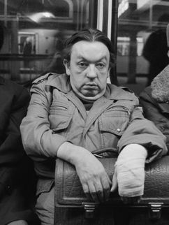 Schwarz-Weiß Fotografie von drei Männern, die eng nebeneinander in einem öffentlichen Verkehrsmittel sitzen. Der mittlere schaut mit skeptischer Miene direkt in die Kamera.