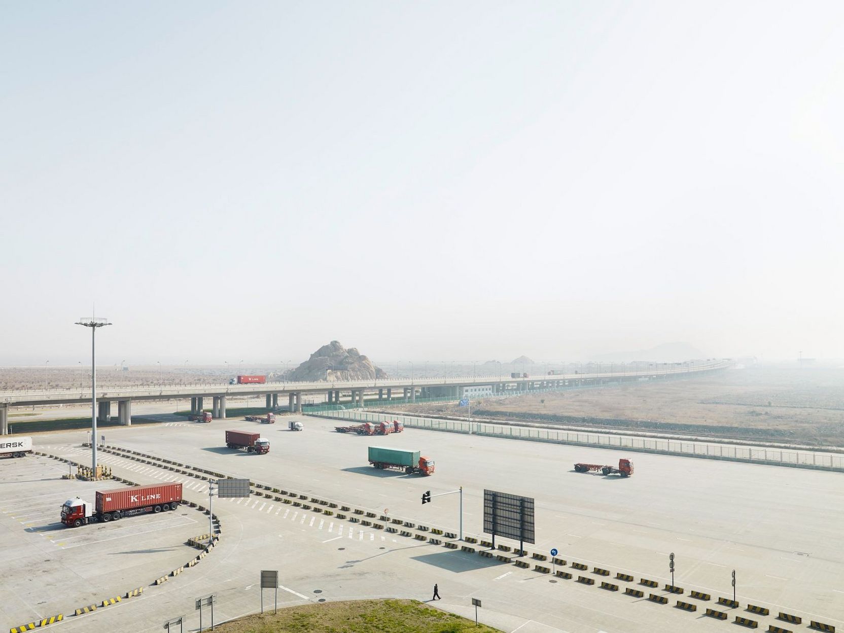 Eine Autobahnstrecke mit vielen Lastwagen durch wüstenartige Landschaft.