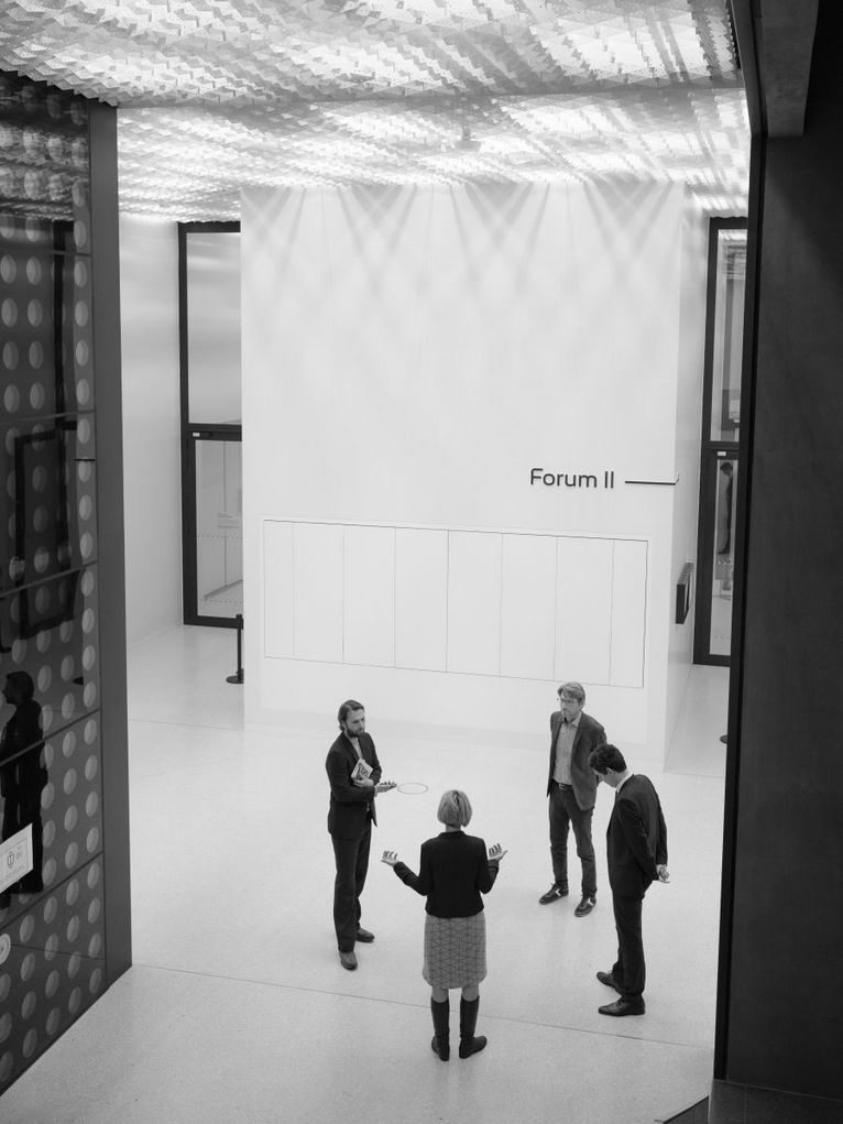 Schwarzweißaufnahme von oben: Swen Schulz, Stefan Brandt, Sunhild Kleingärtner und unser Moderator Frank Steinhofer stehen im Forum II im Futurium, in Berlin. Sie sind im Gespräch.