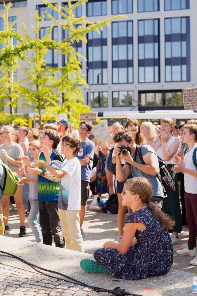 Kinder bei Kundgebung, ein Mann fotografiert ein kleines Mädchen, das auf einer Mauer sitzt.