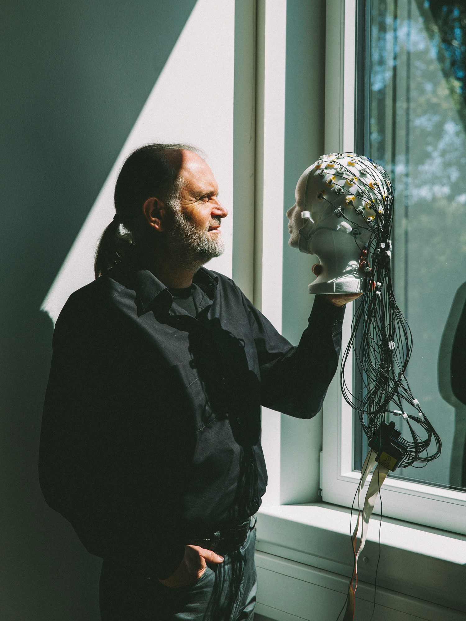 Stephan Getzmann mit Blick aus dem Fenster. Er hält einen verkabelten Puppenkopf in der Hand.