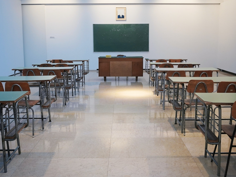 Tische und Stühle vor einer Tafel in einem leeren Klassenraum