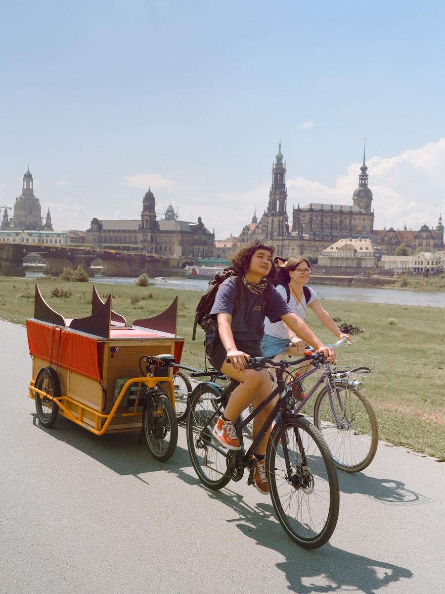 Zwei Fahrradfahrende mit Anhängern vor der Dresdener Altstadtkulisse.