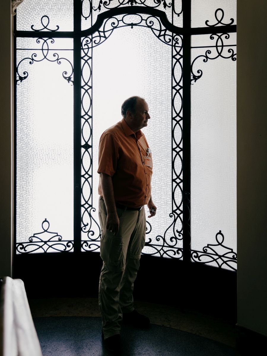 Historiker und Vampirforscher Dr. Peter Mario Kreuter Ein Mann steht im Profil vor einer hohen, ornamentierten Glastür mit schmiedeeisernen Verzierungen. Das Gegenlicht lässt ihn als Silhouette erscheinen. Der Mann ist der Wissenschaftler Peter Mario Kreuter.