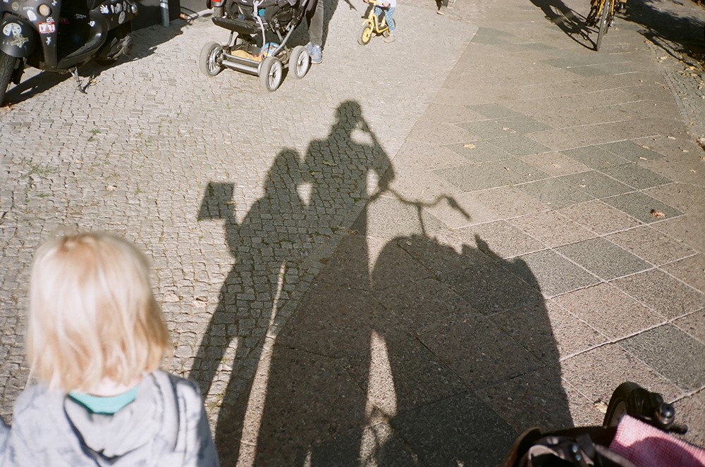 Agnes schaut auf die Schatten, die sie, ihr Vater und ihr Lastenrad auf die Straße werfen.