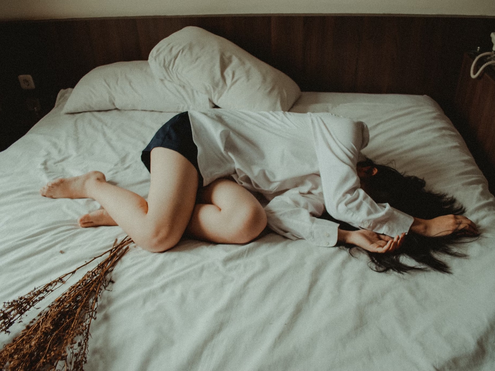 Eine scheinbar unglückliche Frau liegt zusammengekrümmt auf ihrem Bett.
